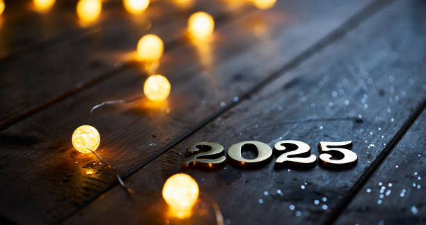 istock The year 2025 is displayed with metallic numbers on a wooden surface, complemented by glowing round string lights and scattered glitter, creating an elegant New Year's setting. 2168800798