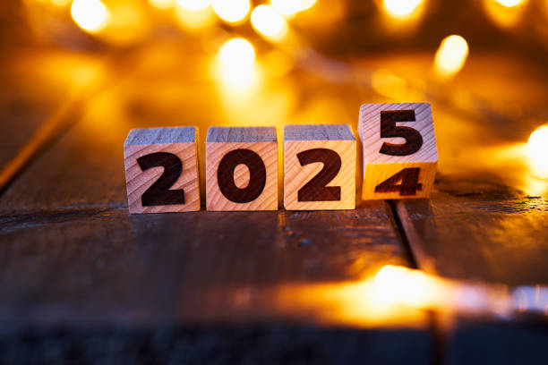 istock Transition from 2024 to 2025 represented by wooden blocks on a rustic surface, illuminated by warm, defocused fairy lights in the background, creating a cozy New Year's Eve atmosphere. 2168800824