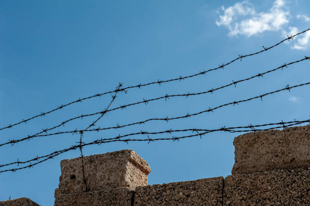 istock Barbed wire fence against blue sky with white clouds 2168805437