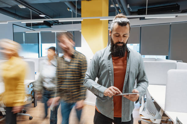 istock Mature entrepreneur using digital tablet in coworking space. Other colleagues passing in motion blur. 2168806236