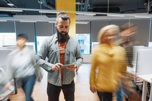 istock Mature entrepreneur using digital tablet in coworking space. Other colleagues passing in motion blur. 2168806308