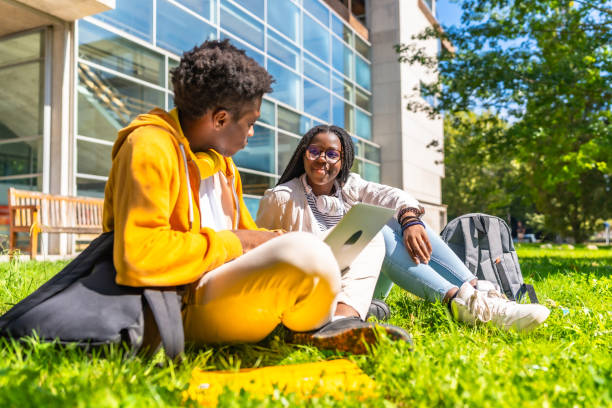 istock University students using laptop sitting on the grass at campus 2168821103