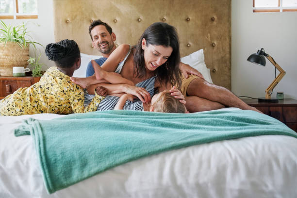 Parents with daughters (18-22 months, 6-7) relaxing on bed