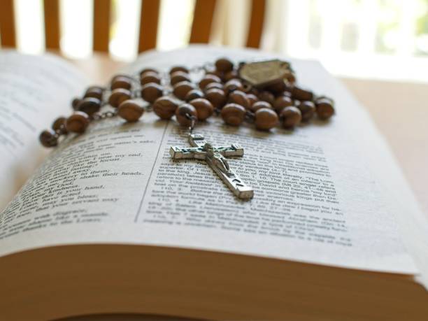 Rosary beads and crucifix lay across scripture text on open bible. Backlit selective focus close-up concept for praying and spirituality.