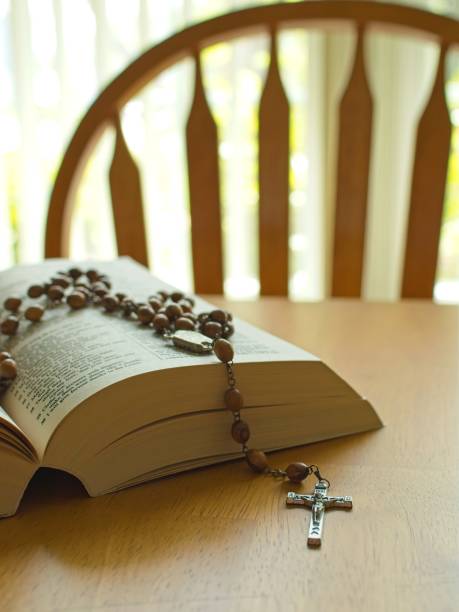 Rosary beads and crucifix lay across scripture text on open bible. Backlit selective focus close-up concept for praying and spirituality.