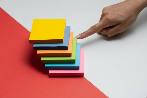 istock Woman hand pointing at the yellow adhesive note from the stack of multicolored adhesive notes against isolated white and red background 2168844628