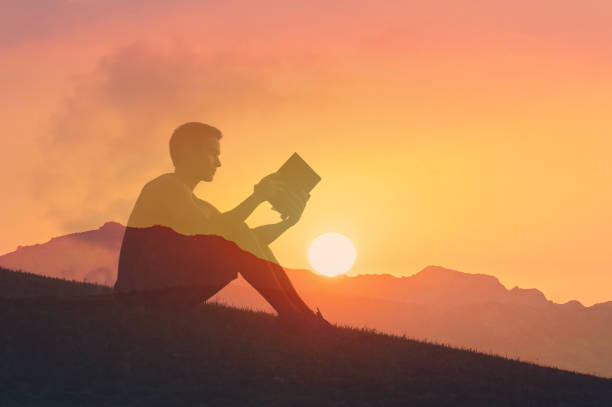 istock Man reading book outside at sunset. 2168846314