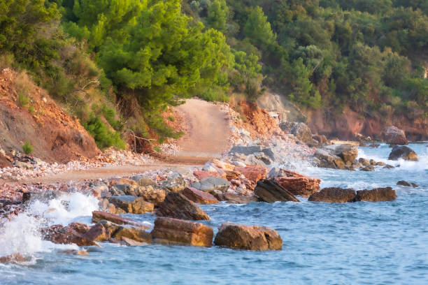 Wild beach Crvena Glavica in Montenegro. Red rocks coast and water waves