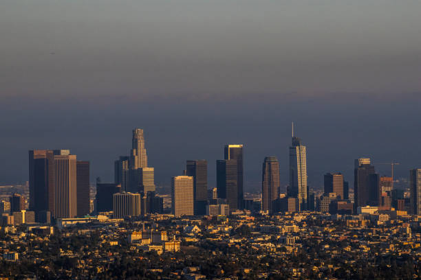 The skyline of downtown Los Angeles on a smoggy day at sunset, with thick gray air pollution behind the skyscrapers of the city