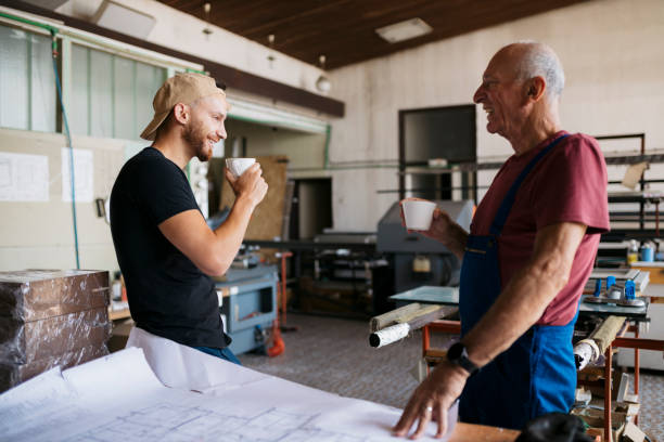 Senior man with young worker taking coffee break at fabrication shop