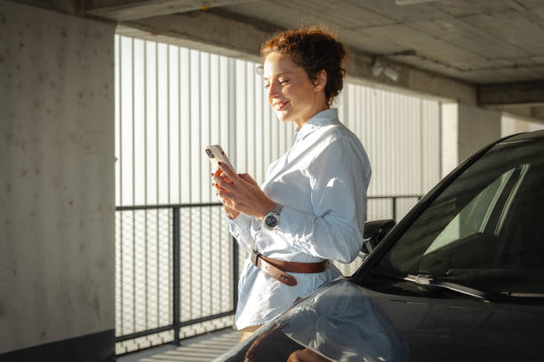 istock Woman leaning on car in parking garage using smartphone 2168876793