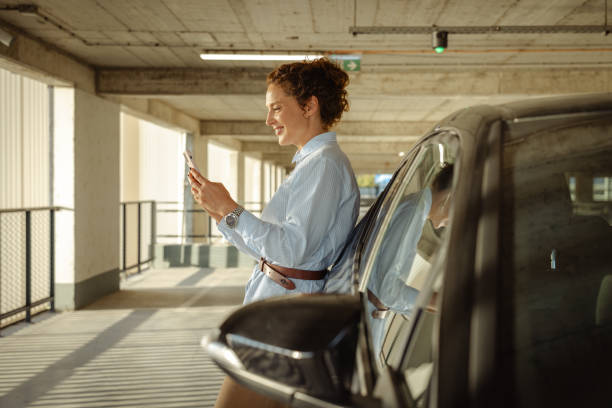 istock Woman leaning on car in parking garage using smartphone 2168876803
