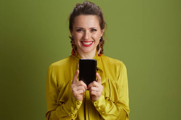 istock smiling trendy woman using smartphone isolated on green 2168879327