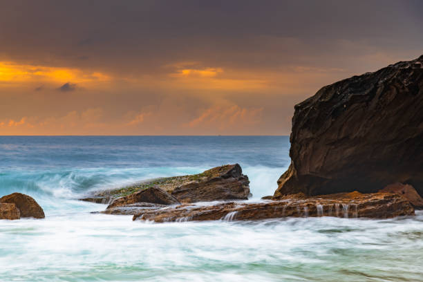 Cloudy sunrise seascape with waves and rocks at Killcare Beach on the Central Coast, NSW, Australia.