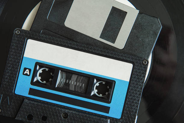 On the vinyl record are a black audio cassette and a floppy disk