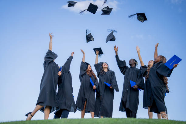 Graduation Cap Toss A large group of university graduates stand together outside as they toss their caps and celebrate their accomplishments. They are each wearing formal black gowns and have joyful expressions on their faces. graduation throwing cap stock pictures, royalty-free photos & images