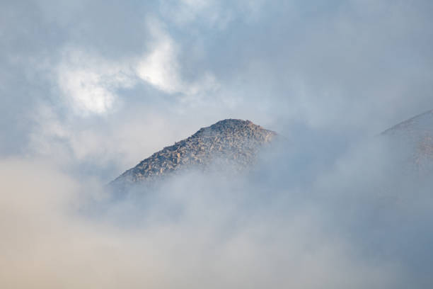 A majestic mountain peak rises above swirling clouds, bathed in soft light as the dawn breaks, revealing a tranquil landscape full of mystery and beauty.