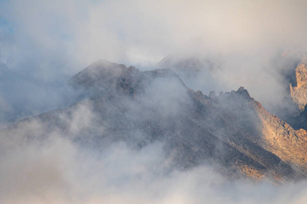 Clouds shroud the majestic mountain landscape at dawn, revealing rugged peaks and creating a serene atmosphere in the remote wilderness.