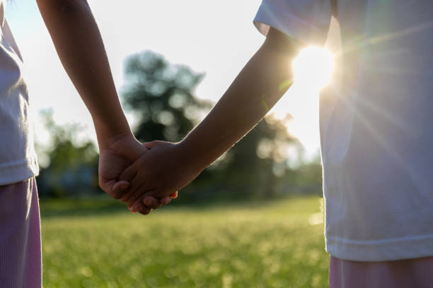 istock Two children holding hands in a grassy field. 2168930125