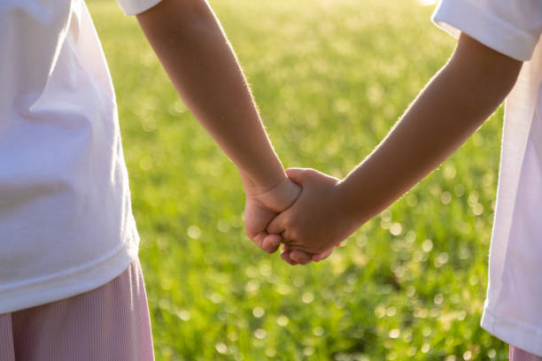 istock Two children holding hands in a grassy field. 2168930133