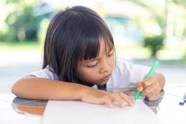 istock A young girl is sitting at a table writing with a pen 2168930626