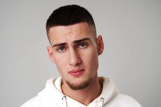 Sad Young Man Looking at Camera against gray background close up