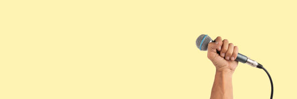 istock Black male hand holding a microphone isolated on light yellow background banner 2168959909