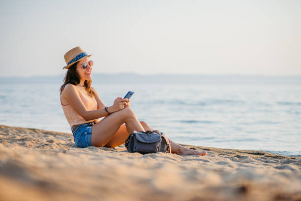 istock Young Woman Using Her Phone While Sitting On The Beach In Neos Marmaras In Greece 2168960582