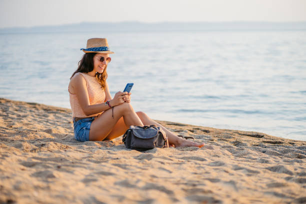 istock Young Woman Using Her Phone While Sitting On The Beach In Neos Marmaras In Greece 2168960751