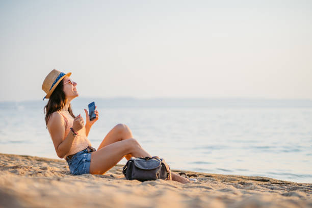 istock Young Woman Using Her Phone While Sitting On The Beach In Neos Marmaras In Greece 2168961000