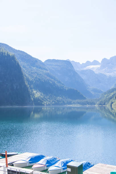 A serene mountain lake surrounded by lush forests and towering peaks. Colorful boats rest quietly at a dock, reflecting the peaceful atmosphere of the natural landscape.