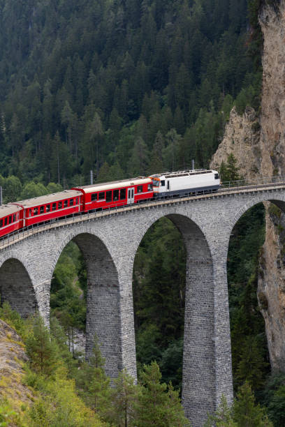 istock Red Train Crossing an Alpine Viaduct Bridge Through Rocky Cliffs 2168980235