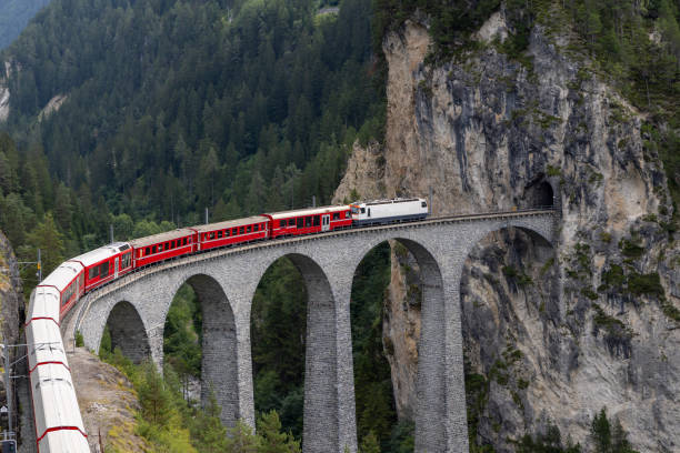 istock Red Train Crossing an Alpine Viaduct Bridge Through Rocky Cliffs 2168980297