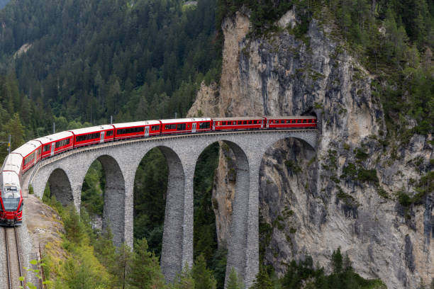 istock Red Train Crossing an Alpine Viaduct Bridge Through Rocky Cliffs 2168980356