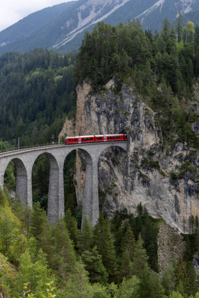 istock Red Train Crossing an Alpine Viaduct Bridge Through Rocky Cliffs 2168980416