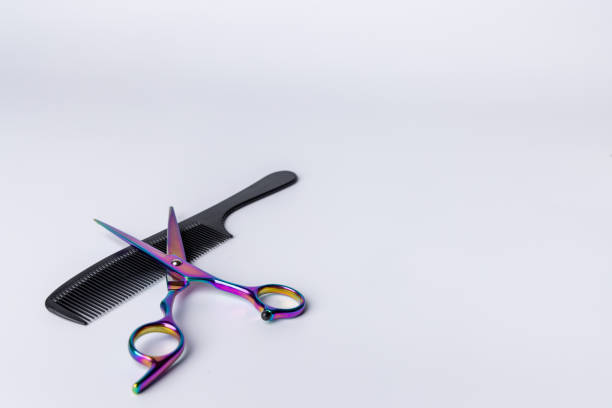 A pair of open scissors resting on a black comb, set against a clean white backdrop. Positioned to the left, perfect for hair styling or barber-related visuals