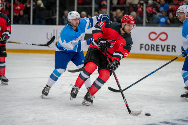 Intense Ice Hockey Action An ice hockey player in a red and black jersey maneuvers the puck as a blue and white team player attempts to block him during a fast-paced game. red hockey jersey stock pictures, royalty-free photos & images