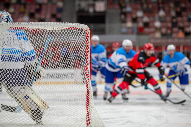 A tense moment on the ice as the goalie prepares to defend against an advancing group of players from both teams, with the focus on the goalie through the net.