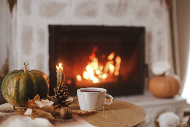 warm cup of tea, pumpkin, autumn leaves on wooden table on background of burning fireplace. cozy autumn still life. thanksgiving and halloween. fall hygge - autumn stockfoto's en -beelden
