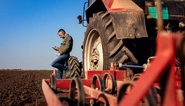 istock Farmer using smart phone while resting after cultivation of soil leaning on tractor tire. 2169001753