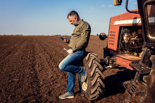 istock Farmer using smart phone while resting after cultivation of soil leaning on tractor tire. 2169001754