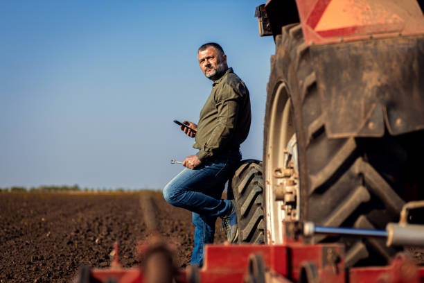 istock Farmer using smart phone while resting after cultivation of soil leaning on tractor tire. 2169001768