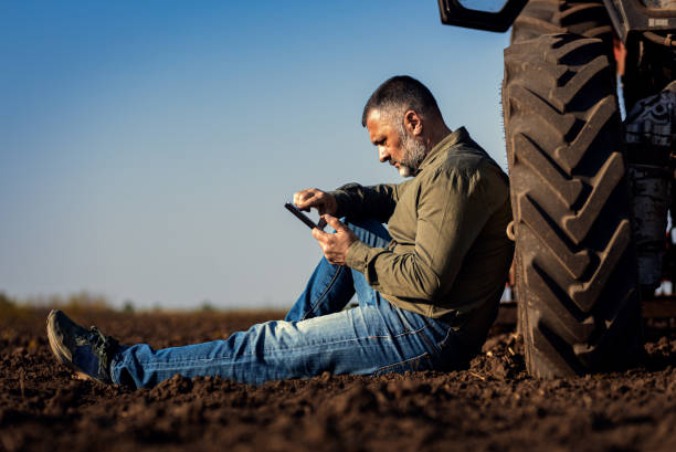 istock Farmer siting and using tablet while resting after cultivation of soil leaning on tractor tire. 2169001830