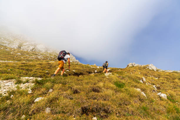 View of a couple with backpacks climbing steep path in the clouds on a summer day, Abruzzo, Italy, Europe