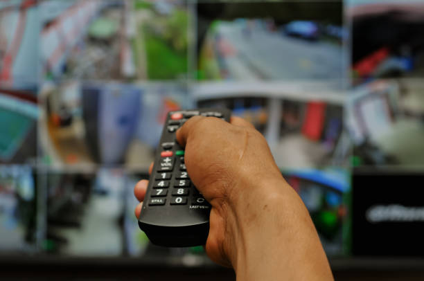 istock a man's hand holding a tv remote, cctv at background 2169019623