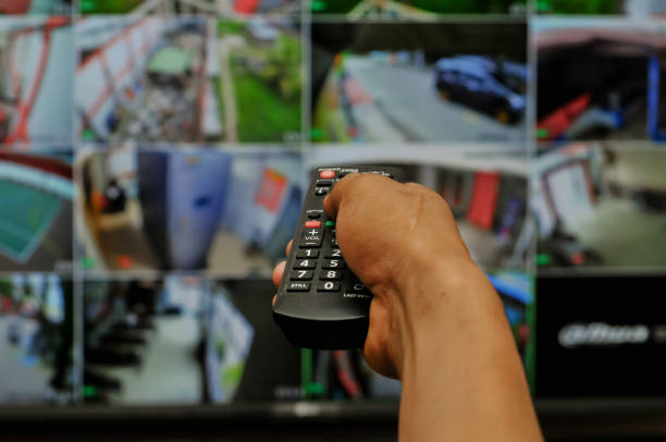 istock a man's hand holding a tv remote, cctv at background 2169019648