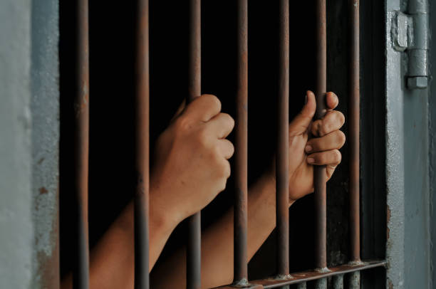 istock hands of a prisoner behind prison bars on black background 2169019689