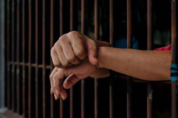 istock hands of a prisoner behind prison bars on black background 2169019744