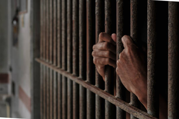 istock hands of a prisoner behind prison bars on black background 2169023588