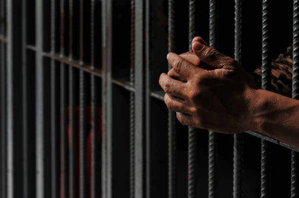 istock hands of a prisoner behind prison bars on black background 2169023640